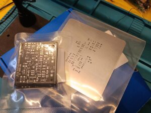 PCB del progetto ProvaTelecomando IR appena ricevuto, ancora nella confezione, affiancato dallo stencil metallico per la deposizione della pasta saldante.
